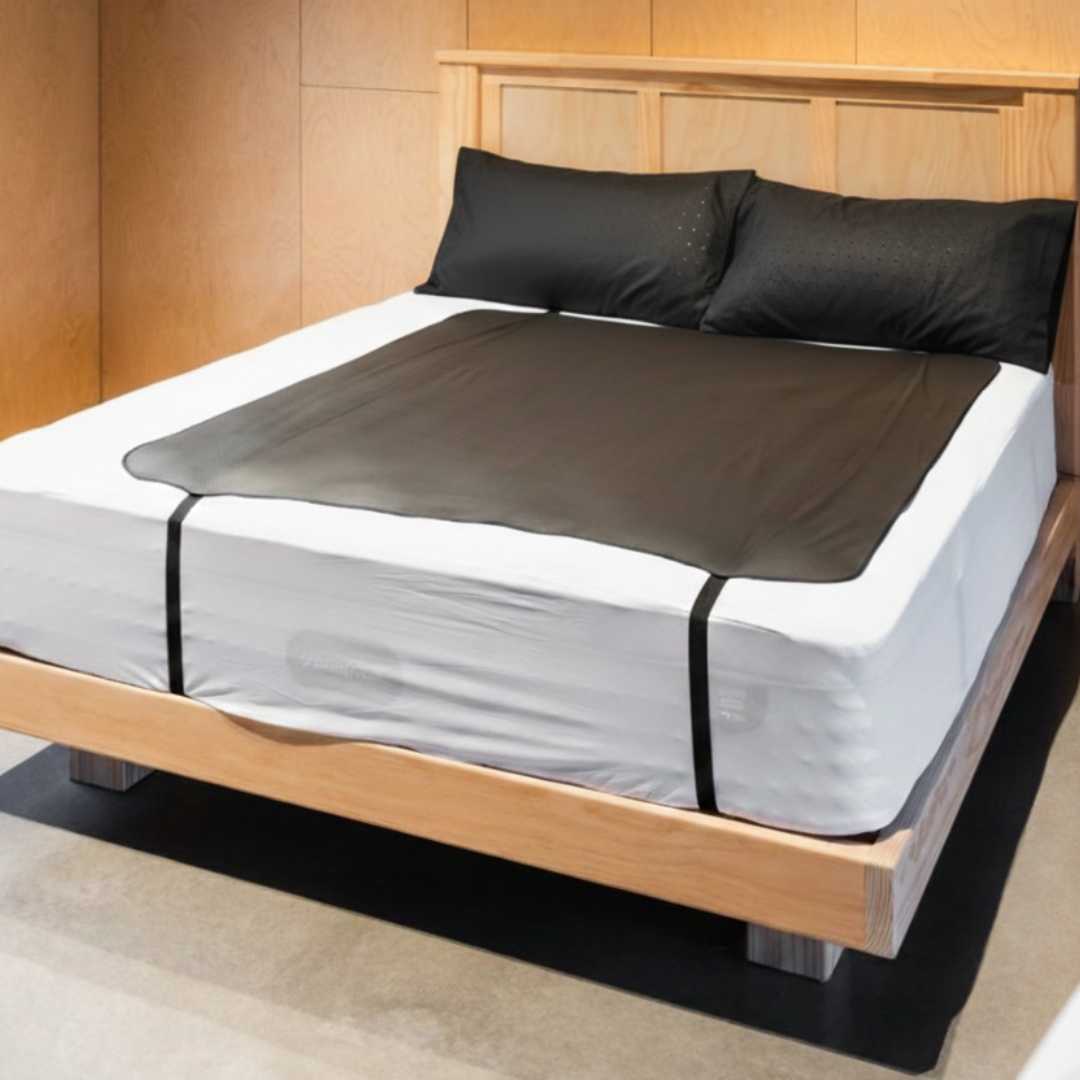 Bed with wooden frame, white mattress, large grounding mat and two pillow covers. 