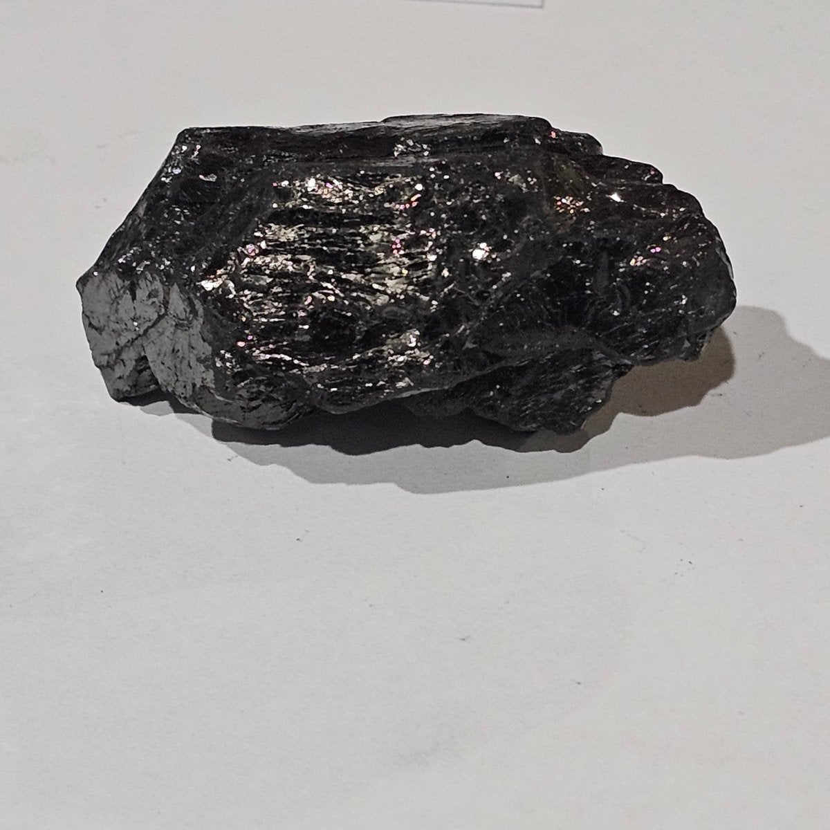 Black mineral sample on a white paper with a wooden surface background