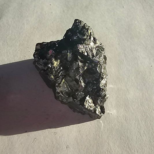 Elite shungite nugget #12, 40.2g: angled black chunk with bright silver and gold glints, casting a shadow