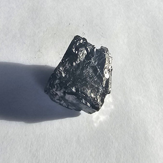 Mount Hicks elite shungite nugget, 13.2g: sunlit squarish chunk with small round silvery spots, crisp shadow