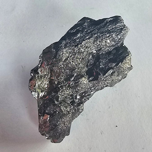 Elite shungite nugget #27, 52g: silvery-grey chunk with flaky layered facets on white paper, desk edge above
