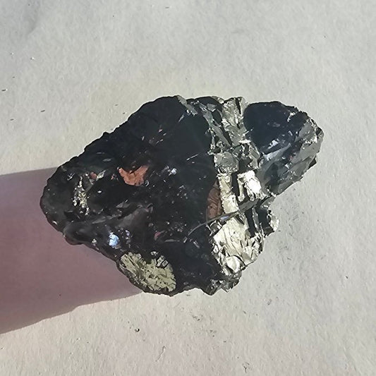 Elite shungite nugget #17, 39.3g: black chunk with silvery and golden flecks balanced on a fingertip over paper