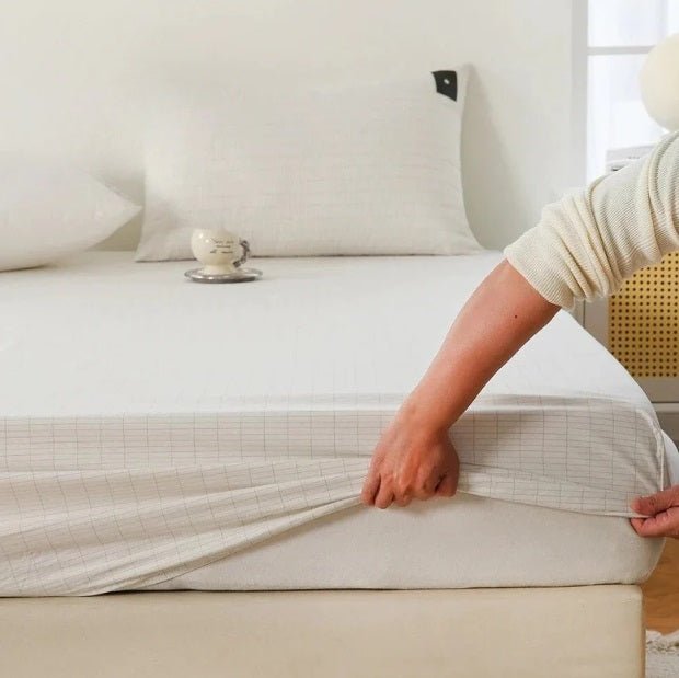 A person is placing an off-white silver fibre grounding sheet on a bed, with a pillow and part of the bed frame visible in the background.
